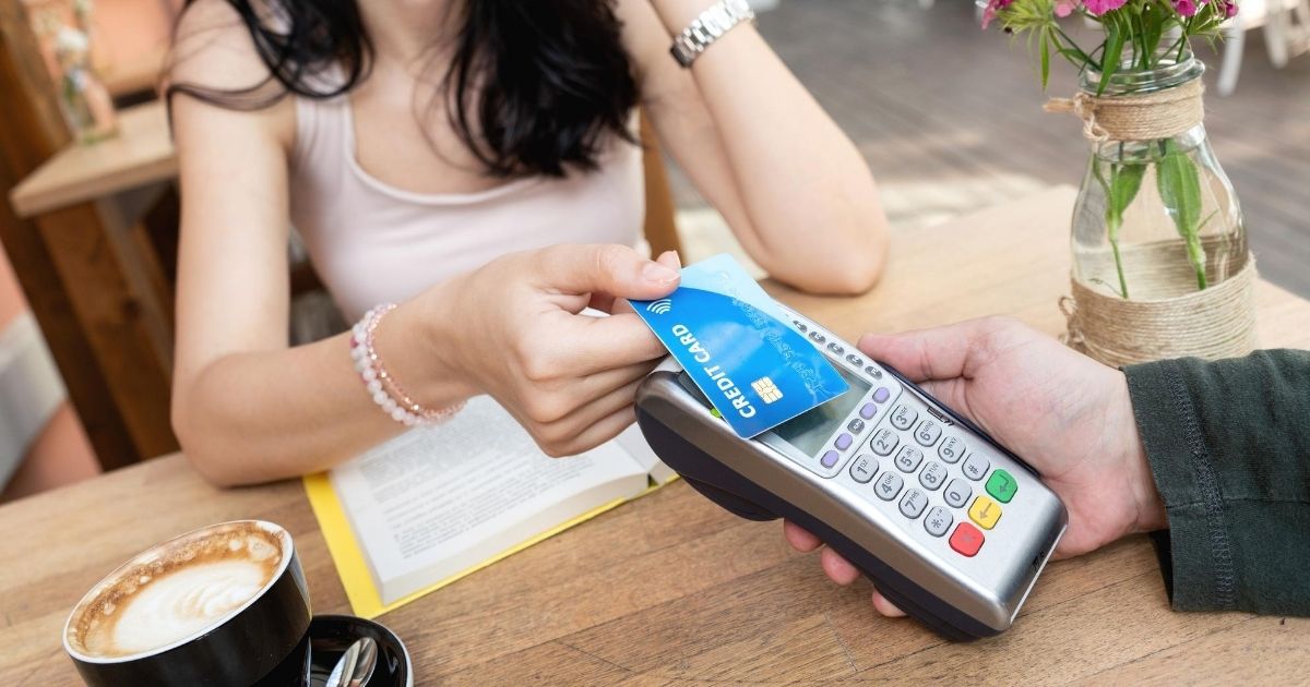 Woman using a credit card with the contactless payment symbol to make a purchase at a cafe